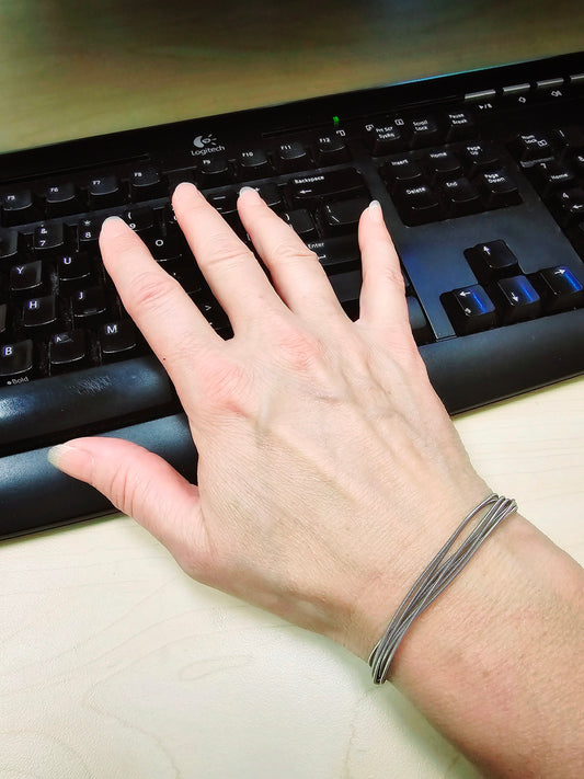 Hand sitting on a black keyboard on wrist is a multi-strand upcycled guitar string bracelet 