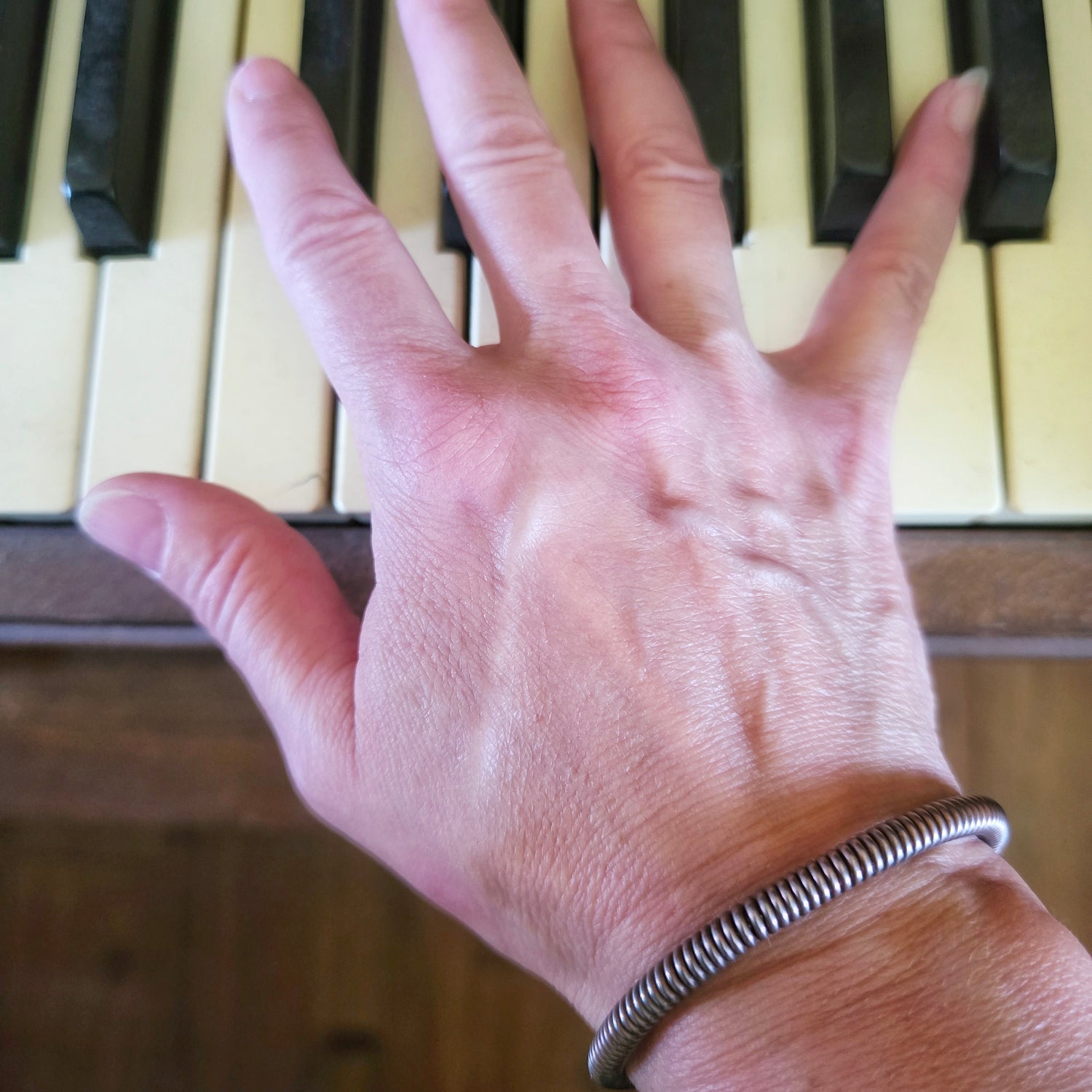 hand on piano keys with upcycled piano string bracelet on wrist