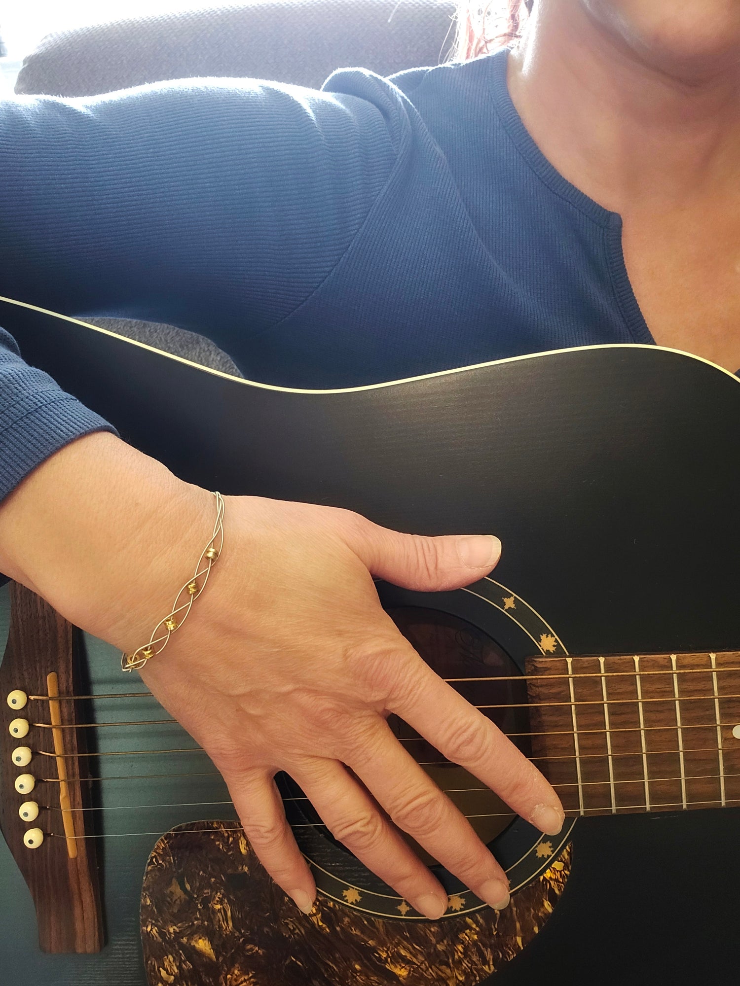 Woman playing guitar wearing upcycled guitar string bracelet