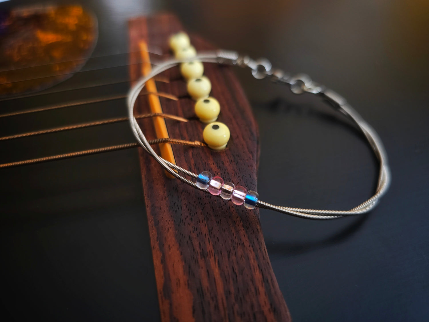 Trans pride guitar string bracelet on black guitar 