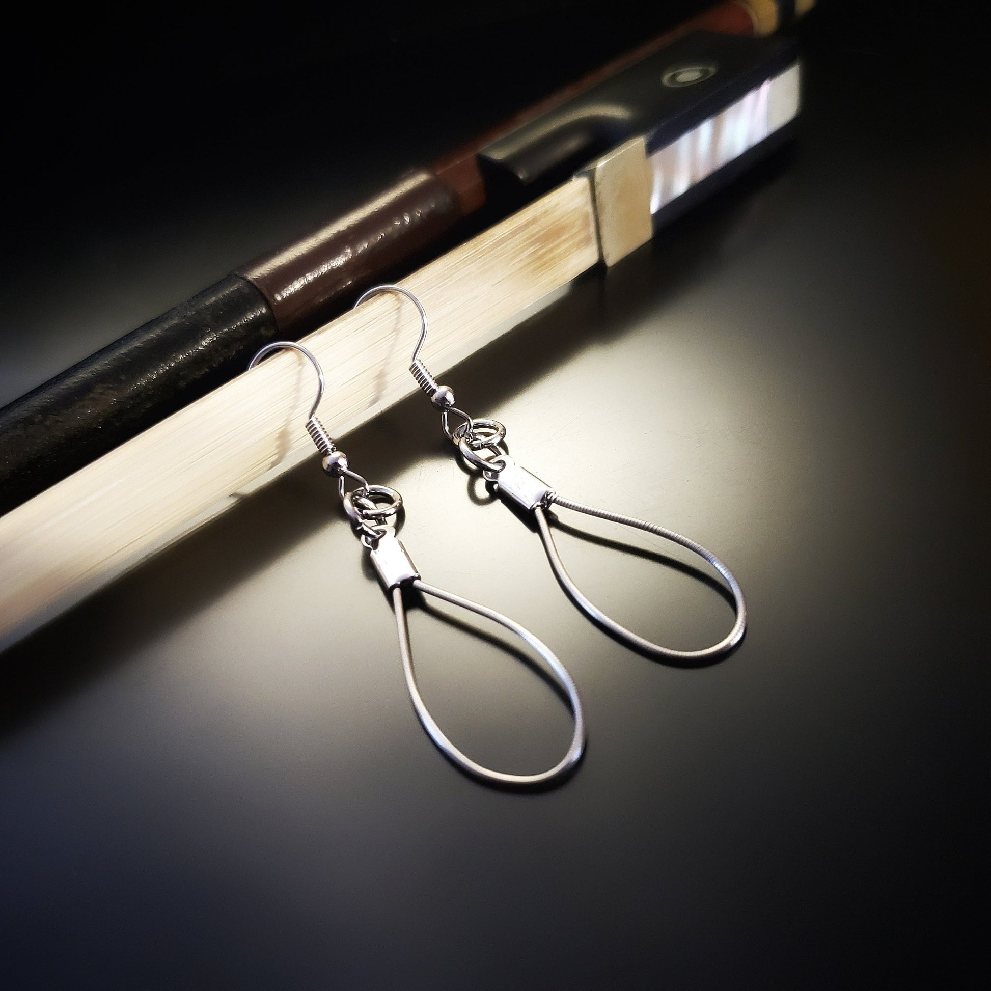 a pair of teardrop style earring made from violin strings hanging off a bow