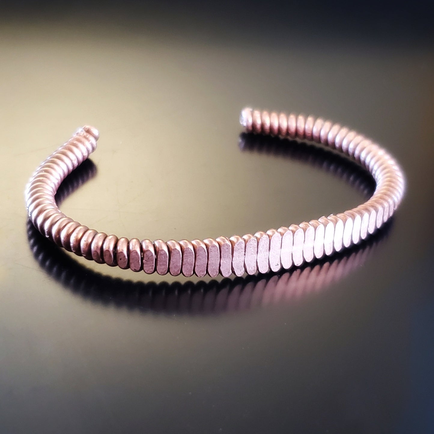 a clasp style bracelet made from an upcycled copper piano string hammered flat 