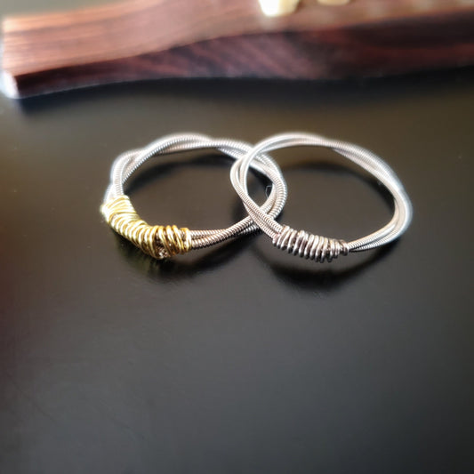 two rings are sitting on a black guitar - both are made from upcycled guitar strings, both are silver but the left one has gold coloured wire and the right one has silver coloured wire