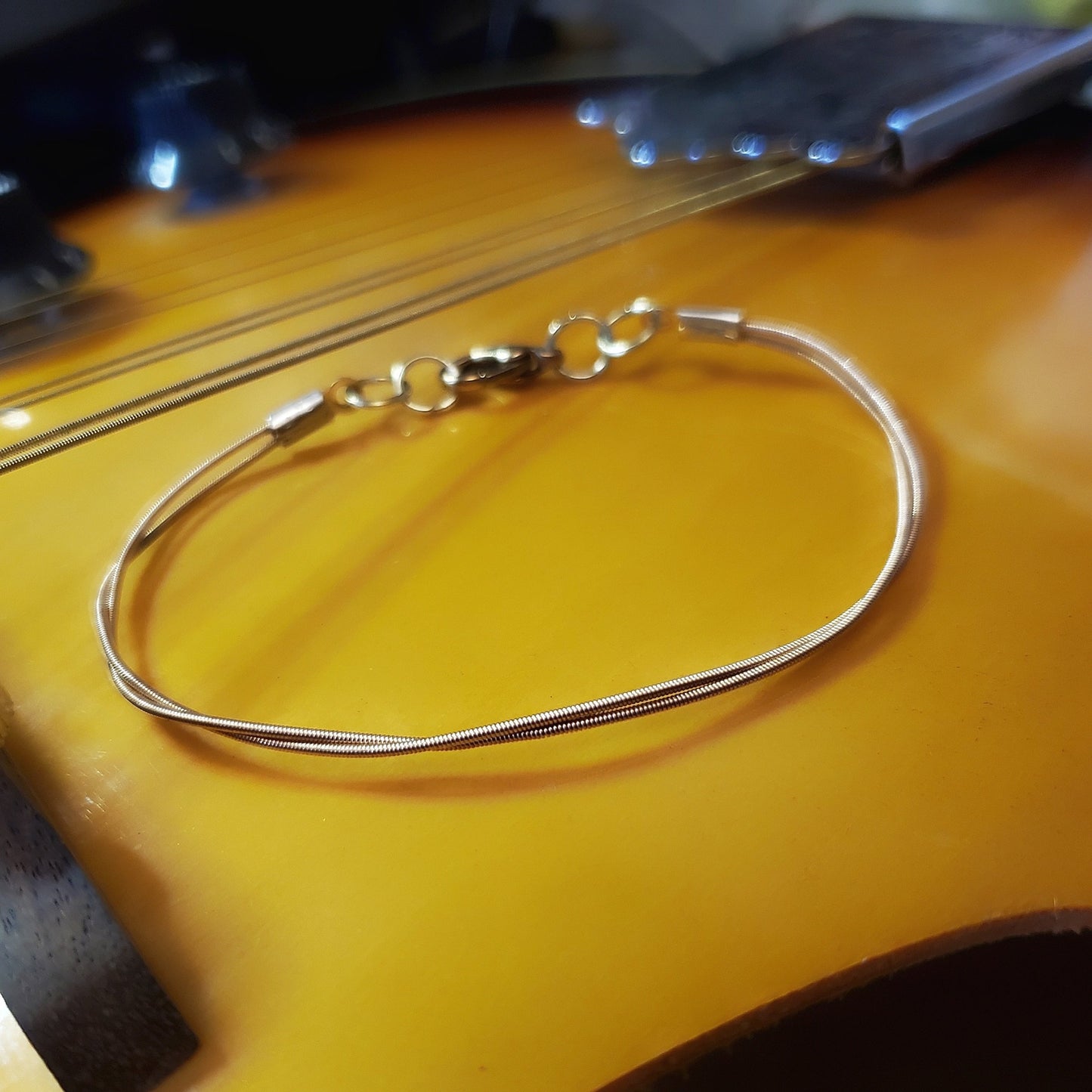 clasp style bracelet made from an upcycled mandolin string sitting on a gold coloured mandolin