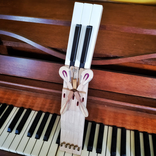 key holder made from 5 upcycled piano keys on the keyholder is a butterfly design made from piano keys and other parts - the key holder is sitting on a piano keyboard