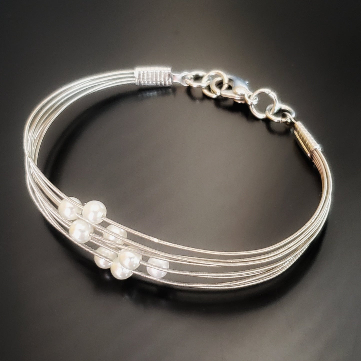 clasp style bracelet made from several strands of upcycled guitar strings on each one is a white glass bead