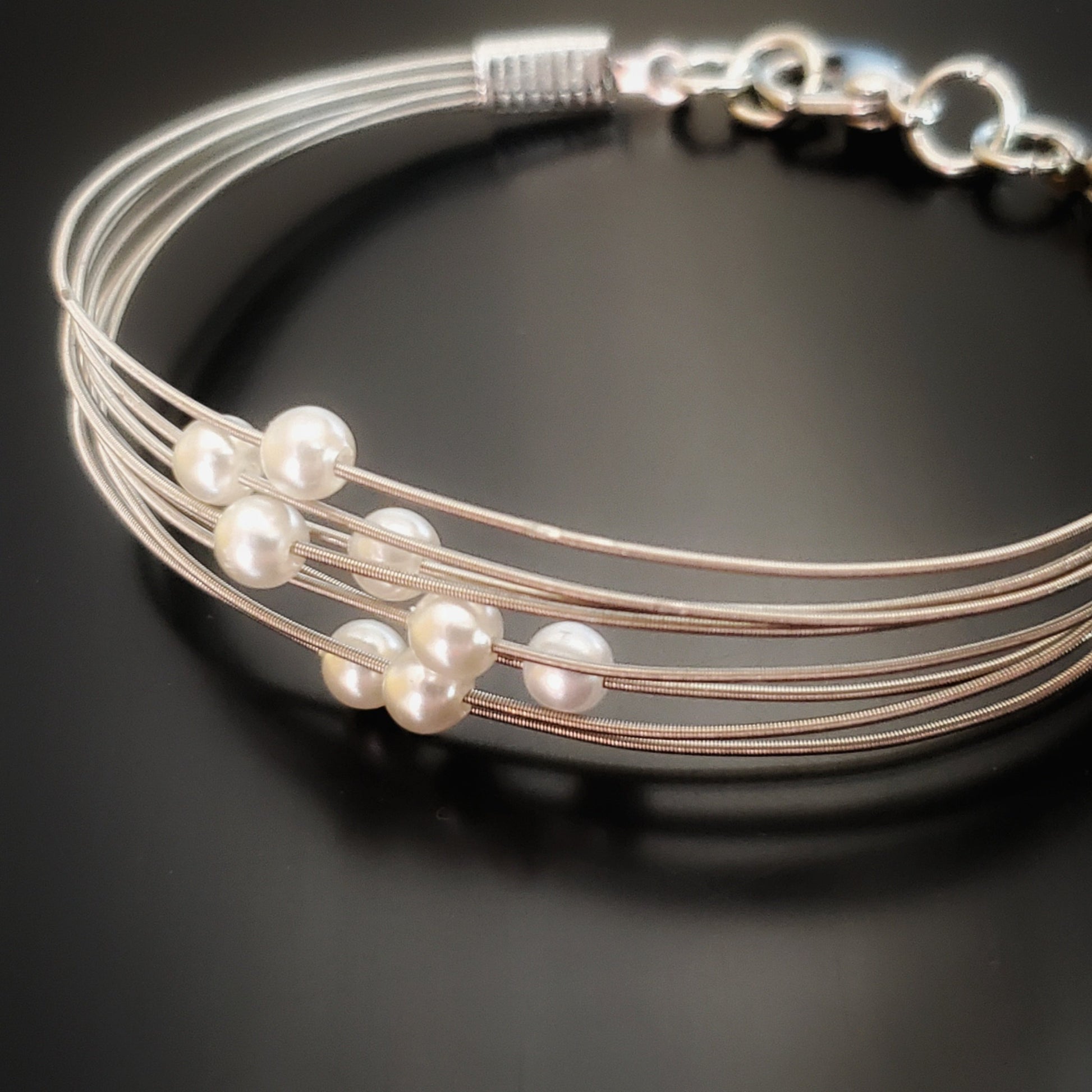 clasp style bracelet made from several strands of upcycled guitar strings on each one is a white glass bead