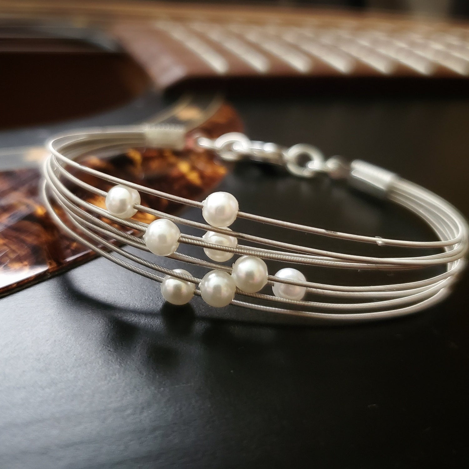 clasp style bracelet made from several strands of upcycled guitar strings on each one is a white glass bead- bracelet is lying on the body of a black guitar