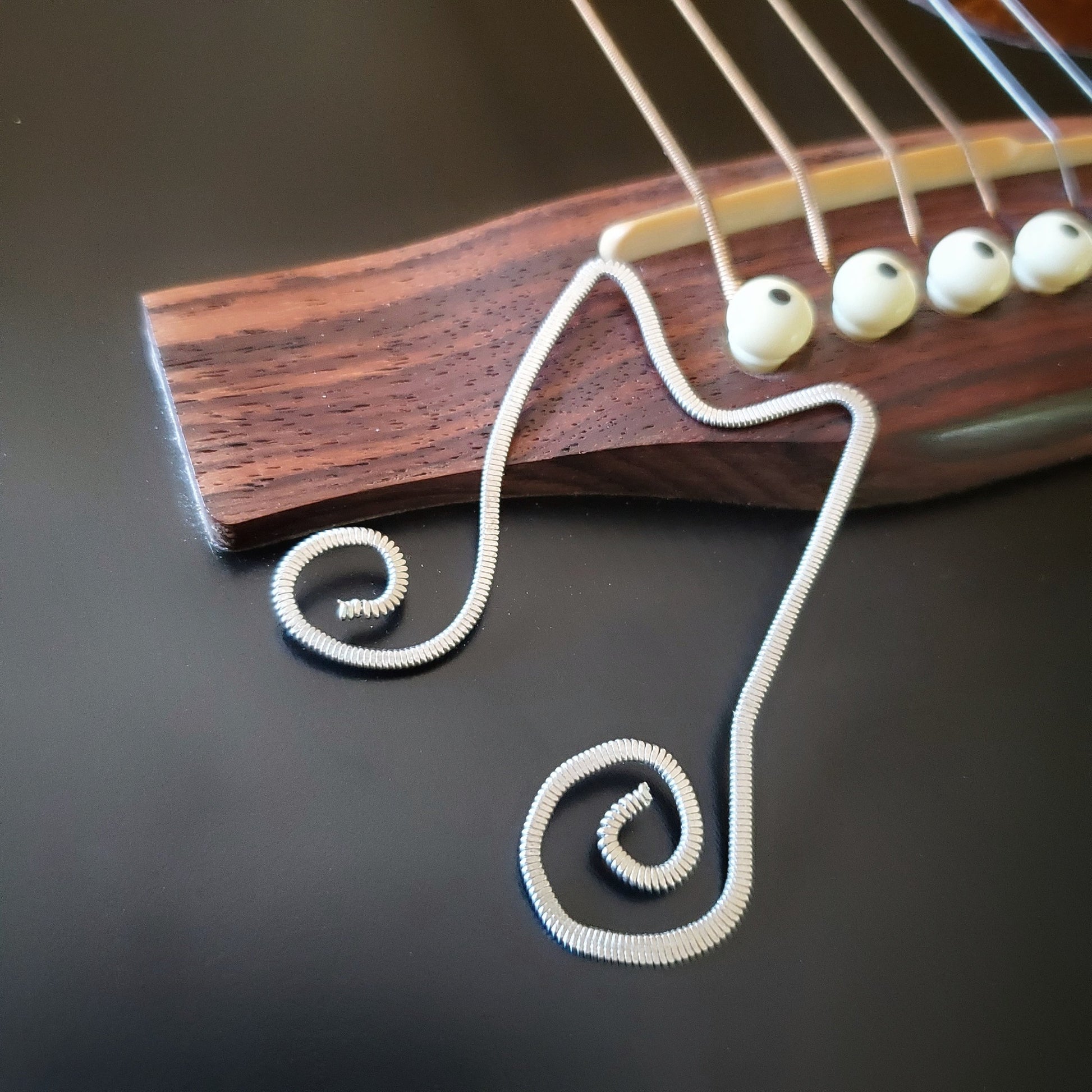 bookmark shaped like a double quarter note made from a hammered guitar string - bookmark is lying on the bridge of a black guitar