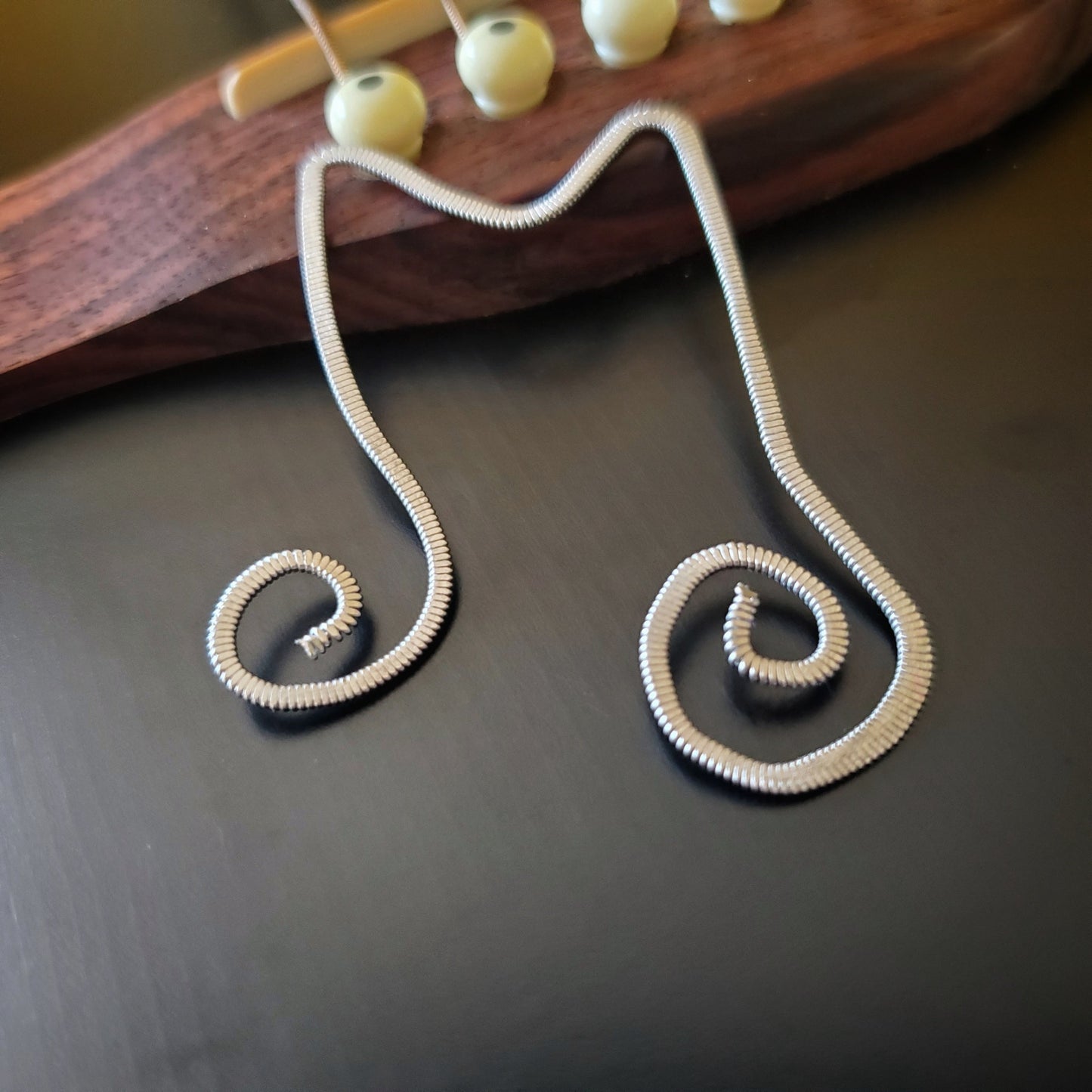 bookmark shaped like a double quarter note made from a hammered guitar string - bookmark is lying on the bridge of a black guitar