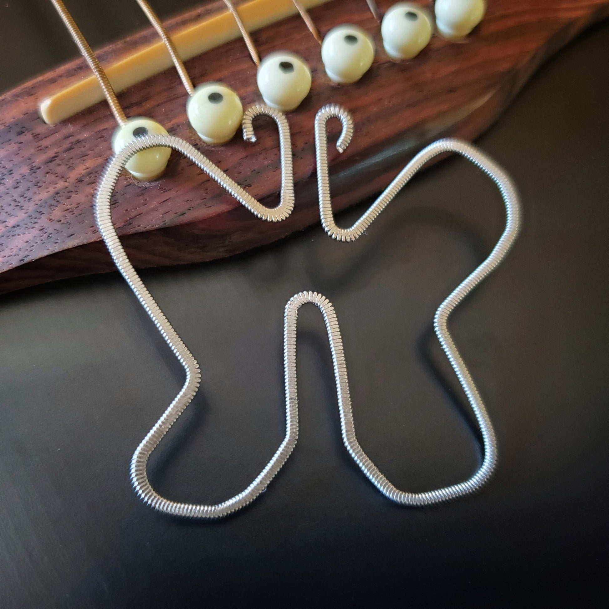 a bookmark made from an upcycled guitar string which was hammered flat and shaped into a butterfly - bookmark sits on the bridge of a black guitar
