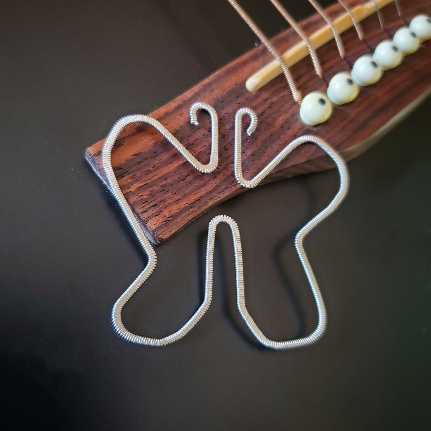 a bookmark made from an upcycled guitar string which was hammered flat and shaped into a butterfly - bookmark sits on the bridge of a black guitar