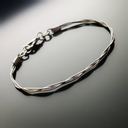 silver coloured bracelet made from 3 cello strings braided together on a black background