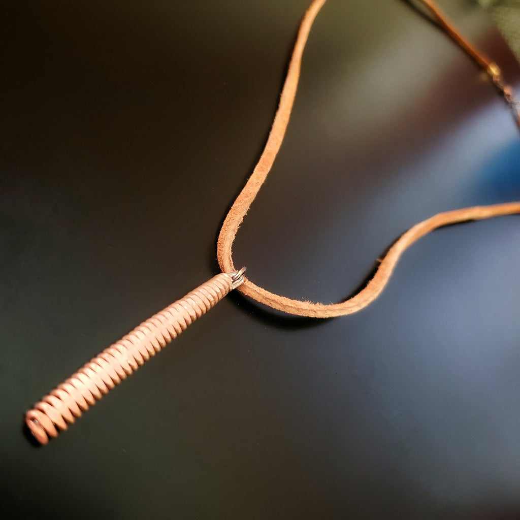 necklace made from a brown suede lanyard on which hangs a pendant made from a copper piano string hammered flat