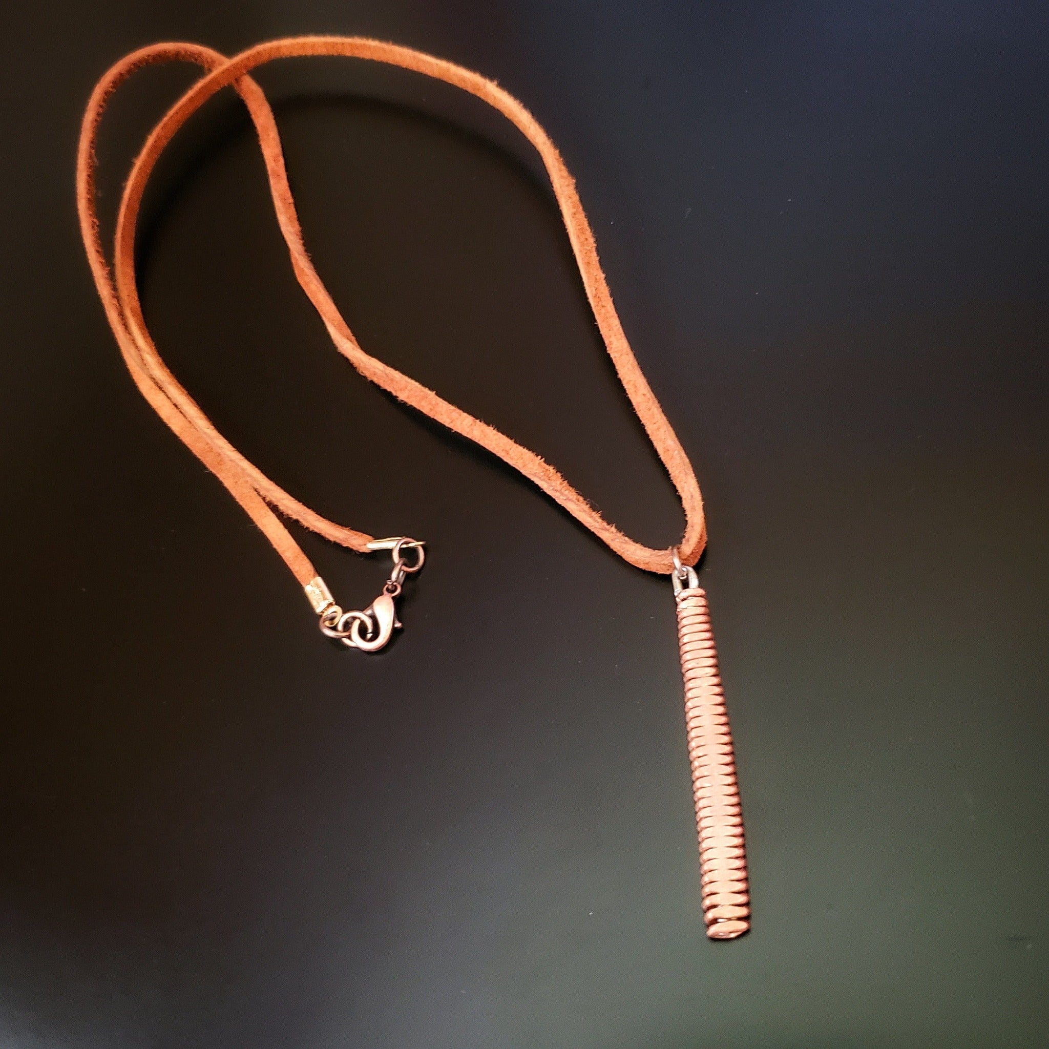 necklace made from a brown suede lanyard on which hangs a pendant made from a copper piano string hammered flat