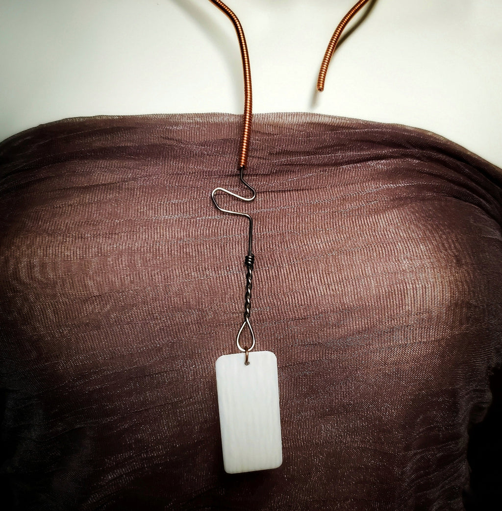 necklace made from an upcycled piano string and an ivory piano key topper - the necklace hangs a white mannequin bust wearing a copper coloured tank style top