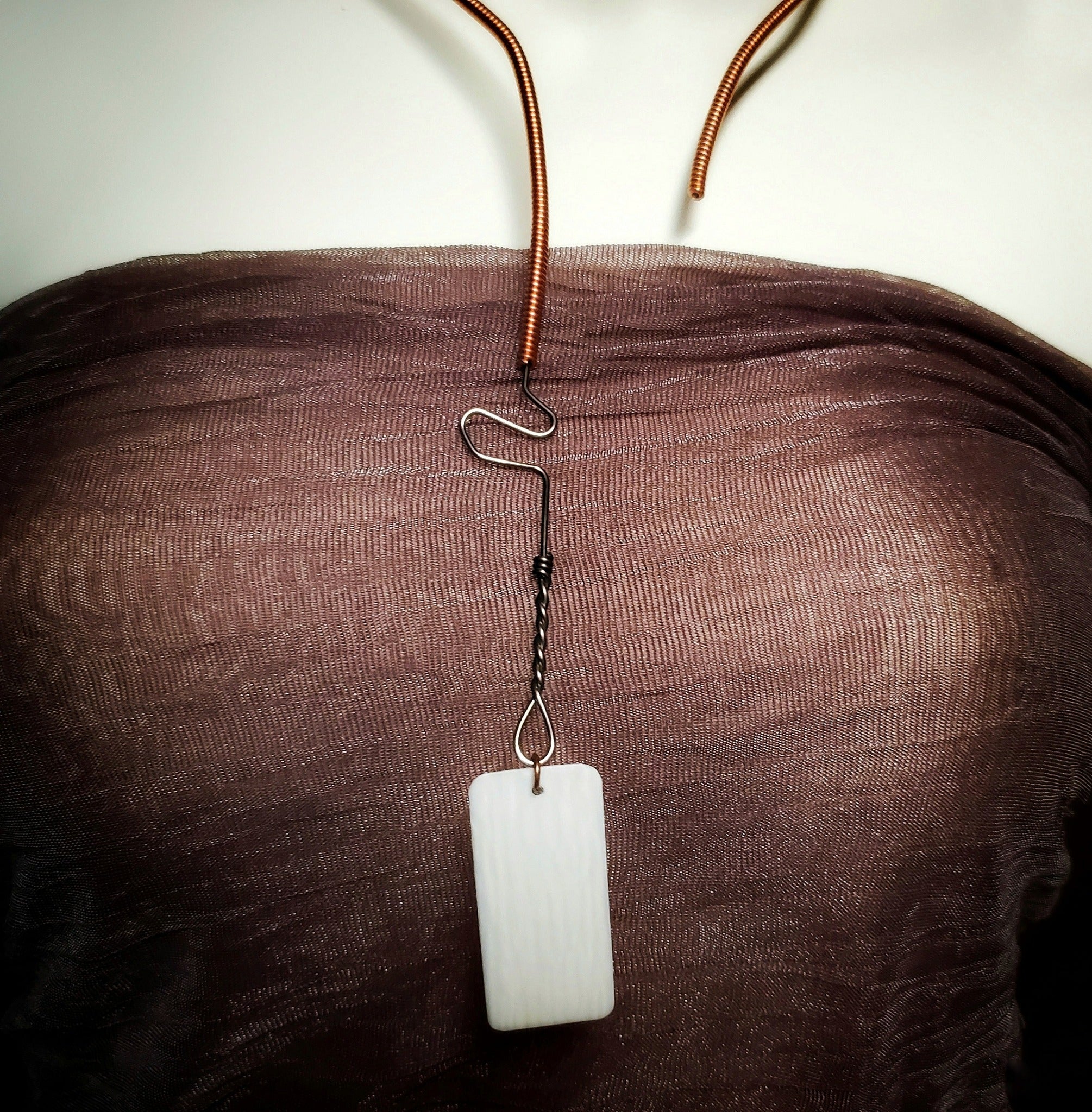 necklace made from an upcycled piano string and an ivory piano key topper - the necklace hangs a white mannequin bust wearing a copper coloured tank style top