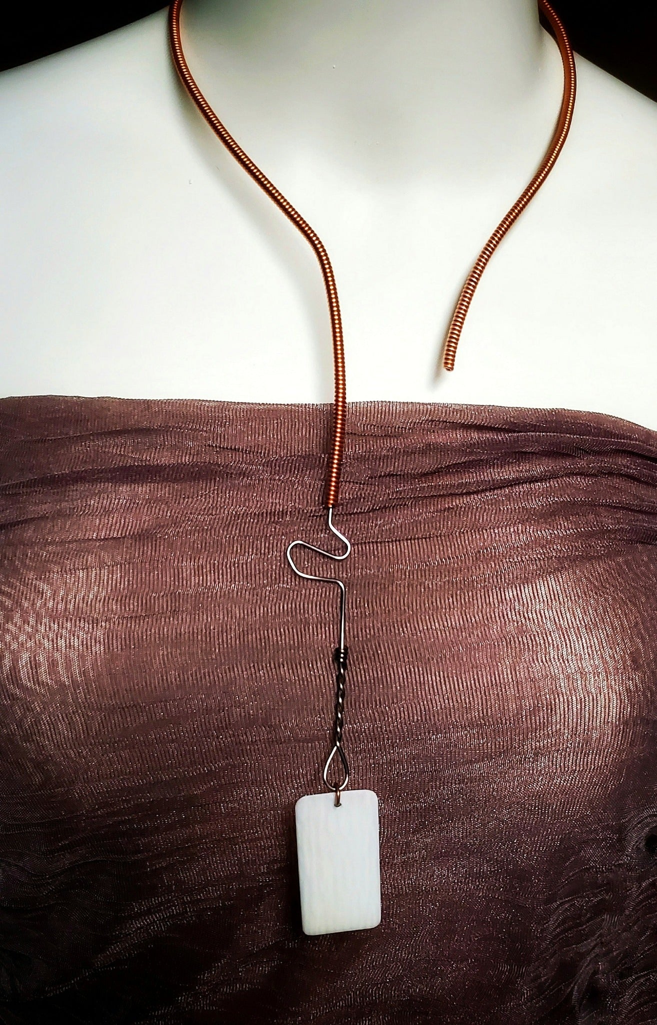 necklace made from an upcycled piano string and an ivory piano key topper - the necklace hangs a white mannequin bust wearing a copper coloured tank style top