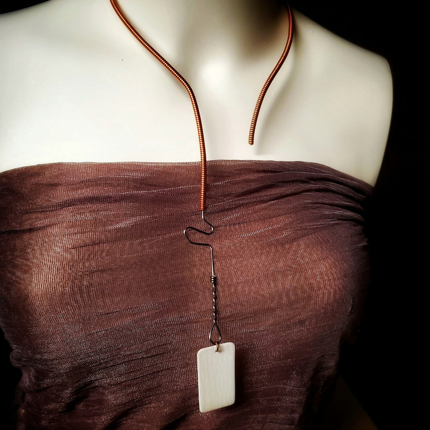 necklace made from an upcycled piano string and an ivory piano key topper - the necklace hangs a white mannequin bust wearing a copper coloured tank style top