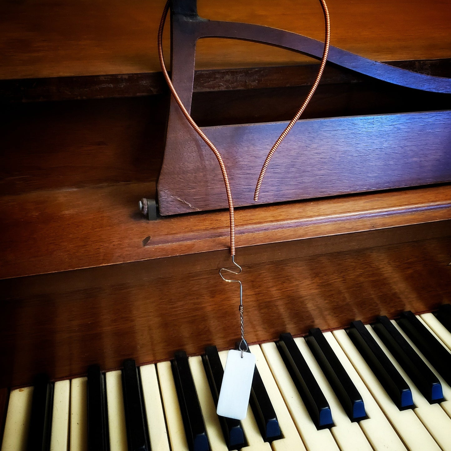 necklace made from an upcycled piano string and an ivory piano key topper - the necklace hangs on the sheet music holder of a piano
