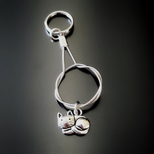a silver coloured keychain made from an upcycled guitar string on which hangs a silver cat pendant - black background with grey shadow