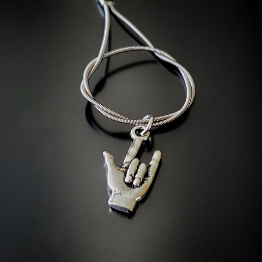 close-up of silver coloured keychain made from an upcycled guitar string on it is hanging a silver coloured pendant in the shape of a hand with the thumb, index and pinky fingers extended