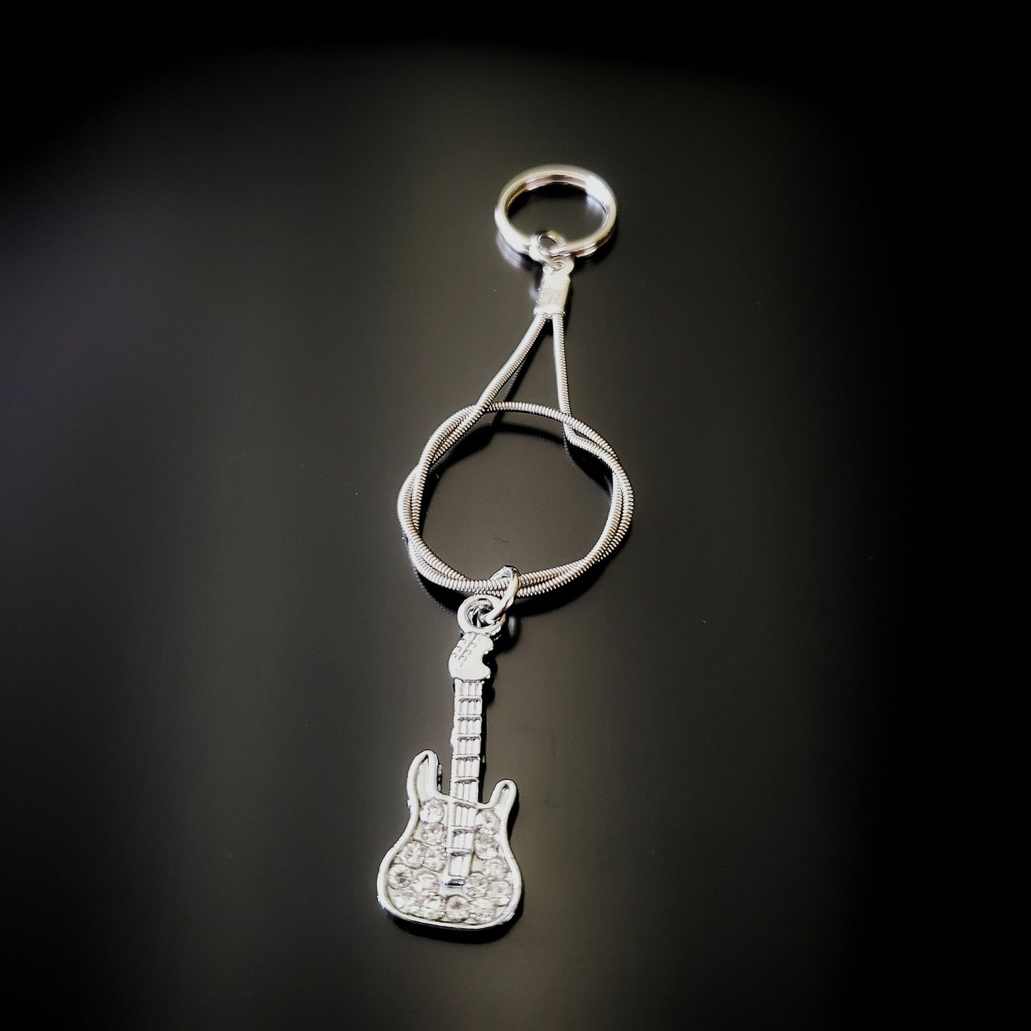 silver coloured keychain made from an upcycled guitar string - on it there is a silver coloured guitar with glass diamonds