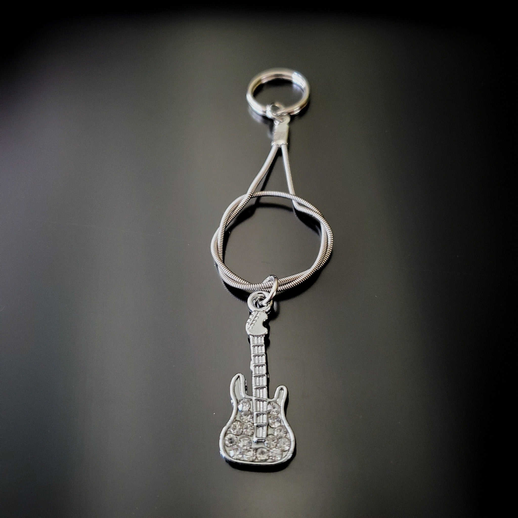 silver coloured keychain made from an upcycled guitar string - on it there is a silver coloured guitar with glass diamonds