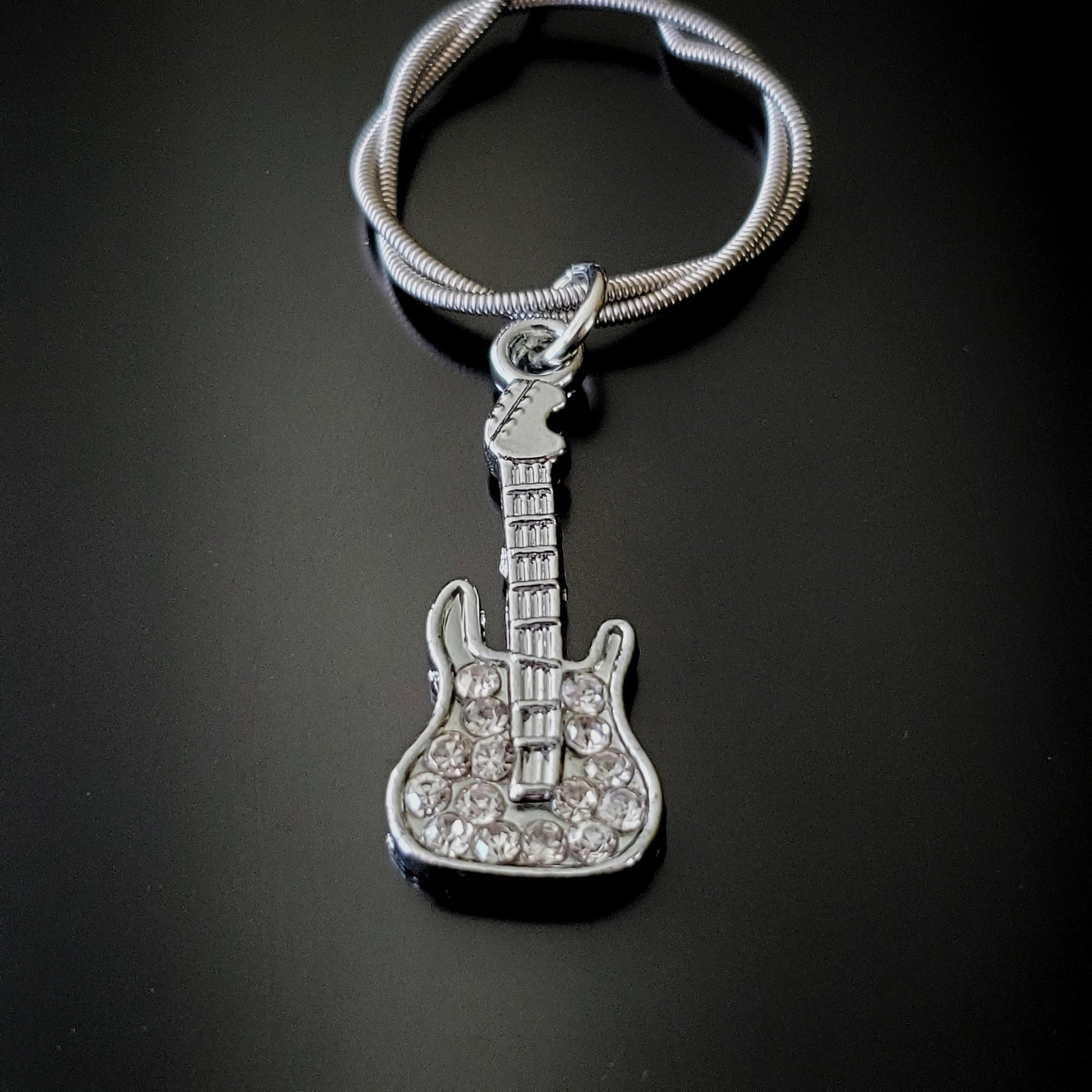 close-up of silver coloured keychain made from an upcycled guitar string - on it there is a silver coloured guitar with glass diamonds
