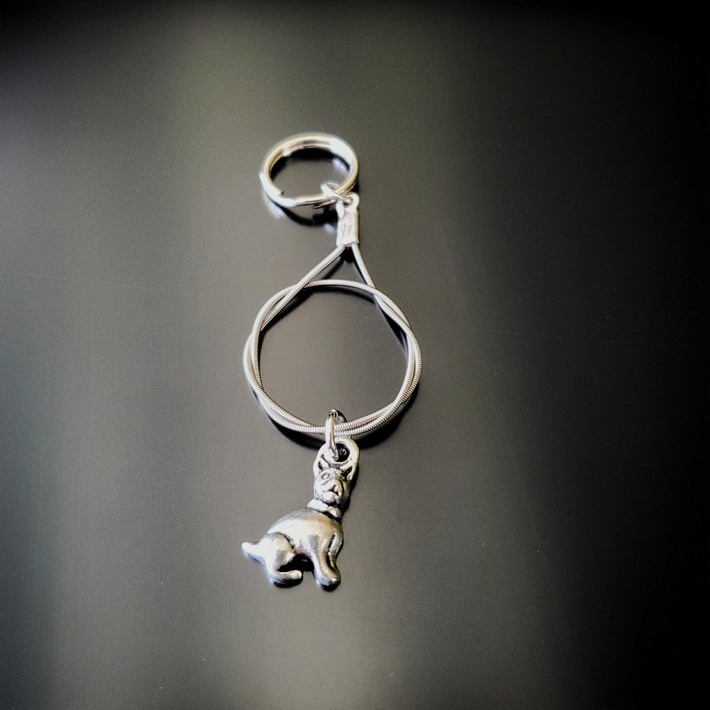 a silver coloured keychain made from an upcycled guitar string on which hangs a silver dog pendant - black background with grey shadow
