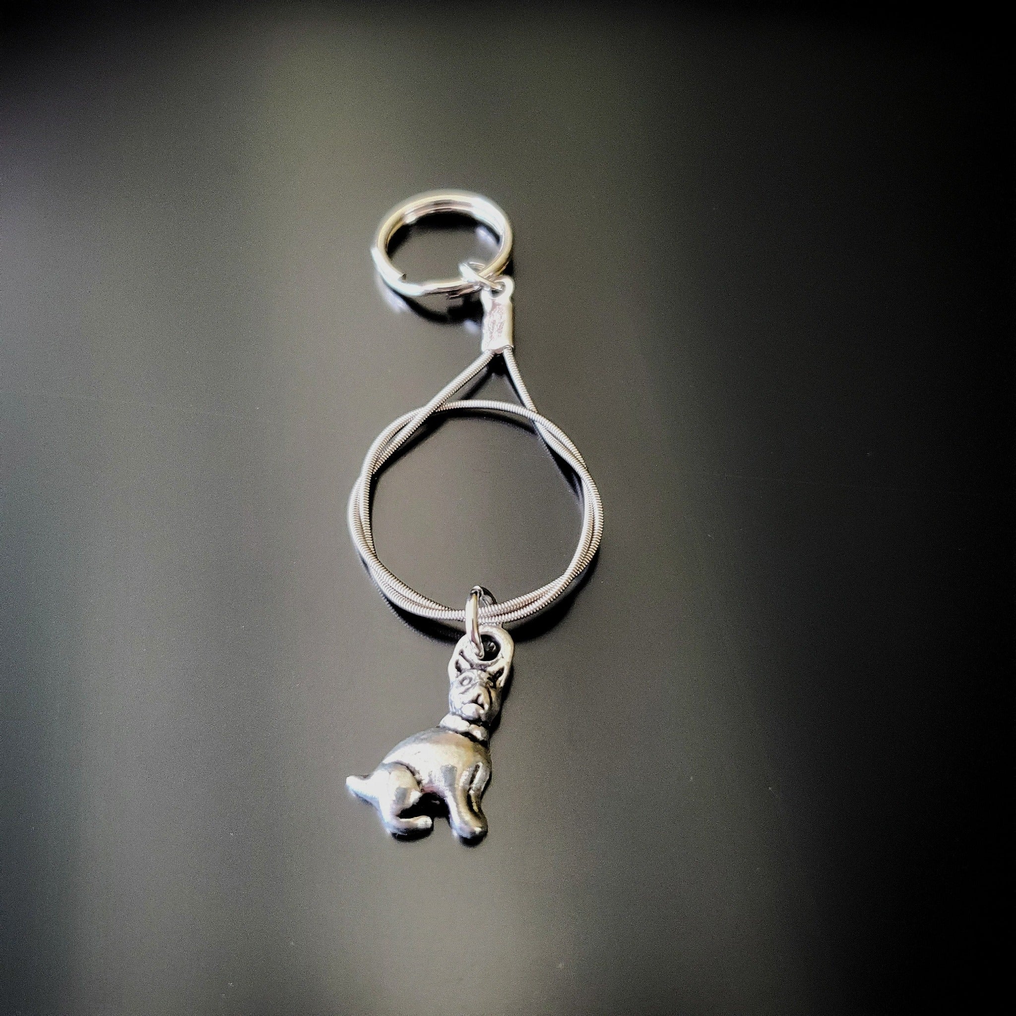 a silver coloured keychain made from an upcycled guitar string on which hangs a silver dog pendant - black background with grey shadow