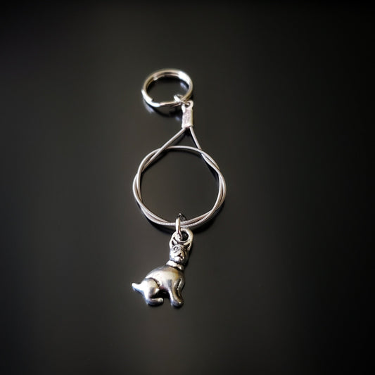 a silver coloured keychain made from an upcycled guitar string on which hangs a silver dog pendant - black background with grey shadow