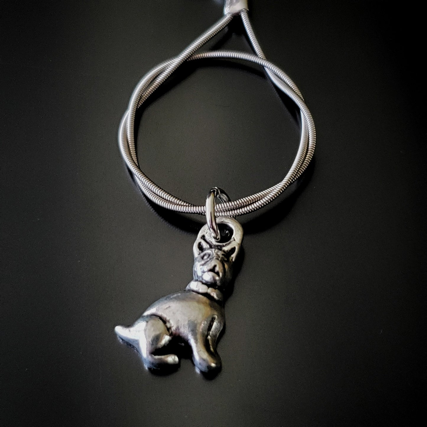 close up of a silver coloured keychain made from an upcycled guitar string on which hangs a silver dog pendant - black background with grey shadow