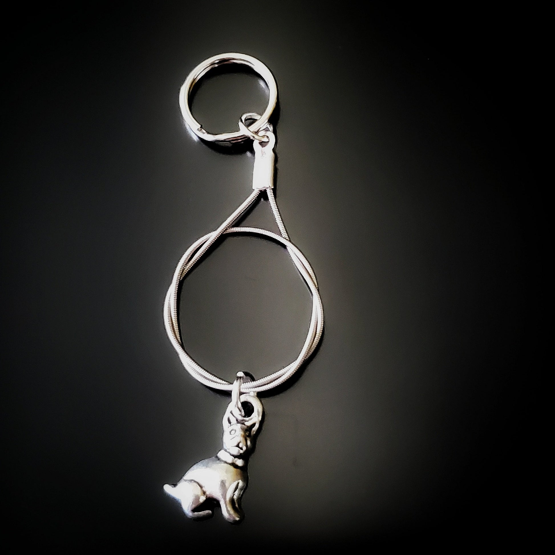 a silver coloured keychain made from an upcycled guitar string on which hangs a silver dog pendant - black background with grey shadow