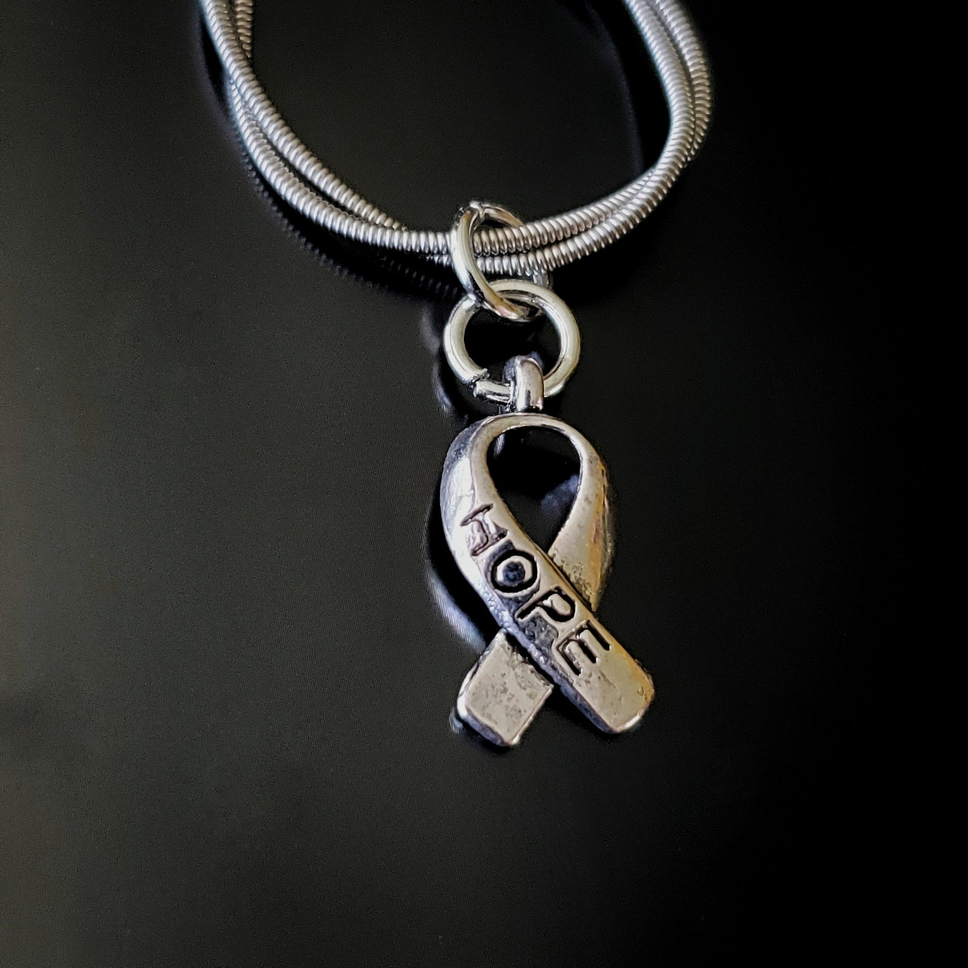 close-up of a silver coloured keychain made from an upcycled guitar string with a silver coloured ribbon shaped charm with the word HOPE etched on it