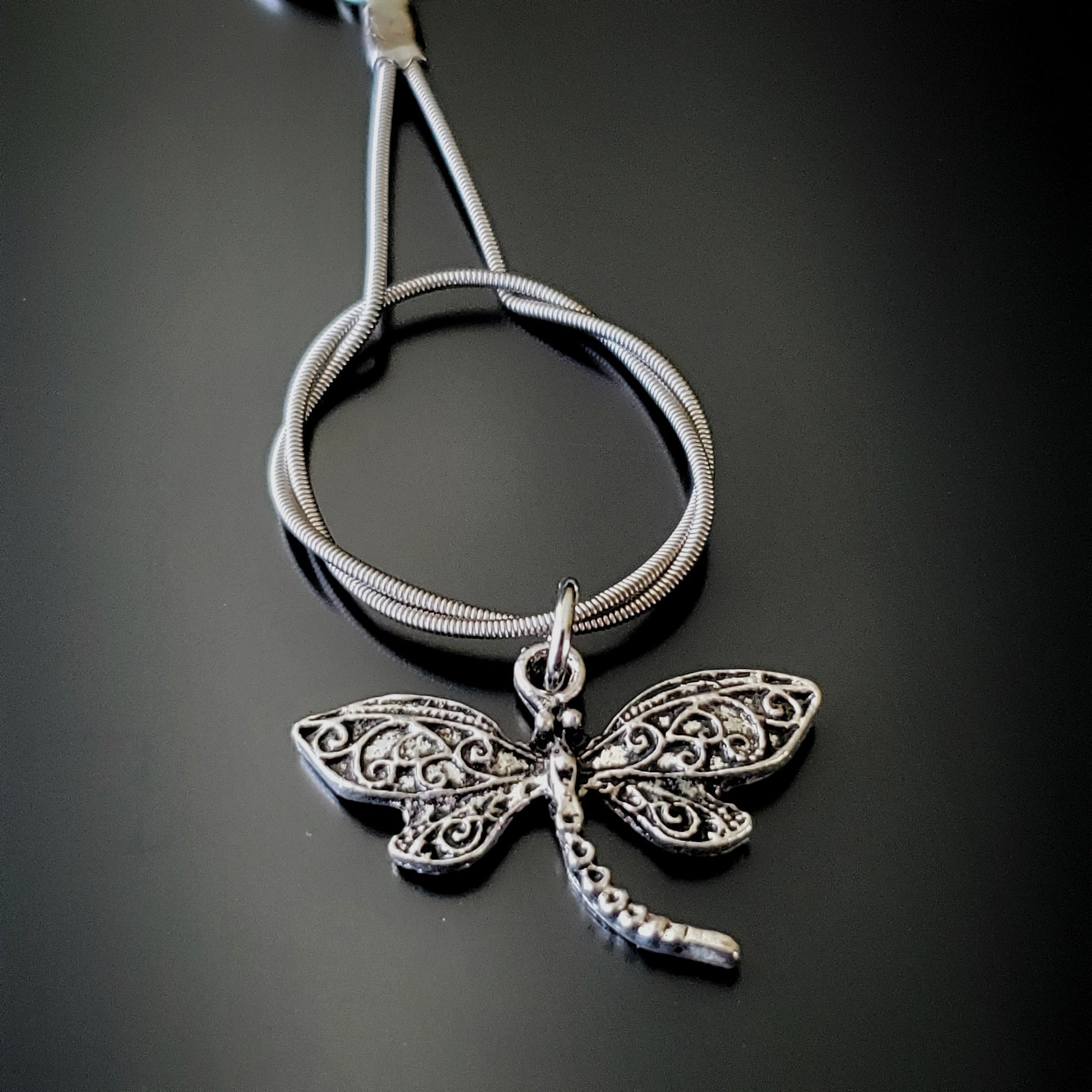 closeup of a silver coloured keychain made from an upcycled guitar string on which hangs a silver coloured dragonfly pendant