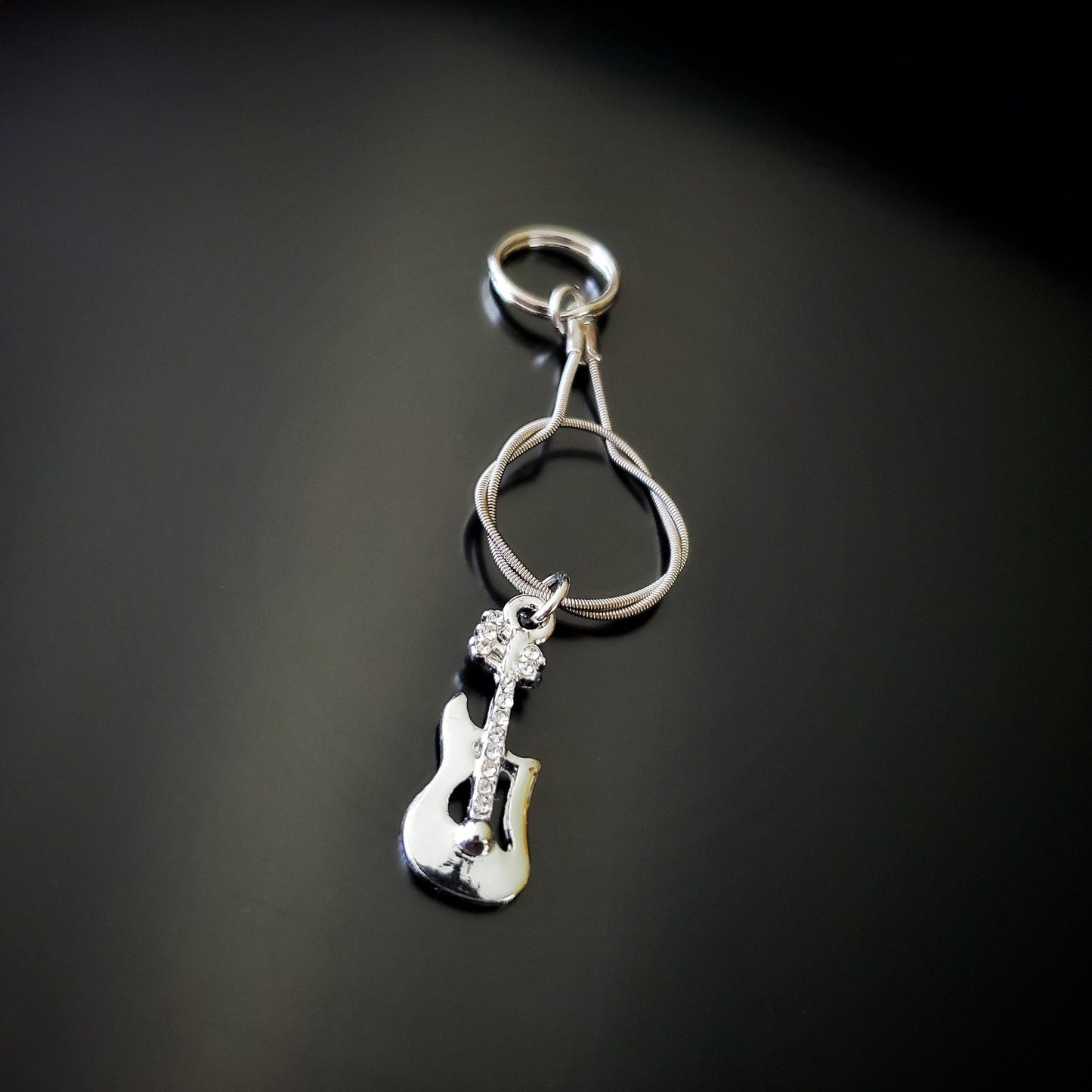 silver coloured keychain made from an upcycled guitar string - on it hangs a silver coloured electric guitar