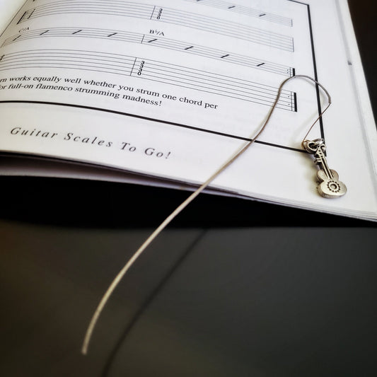 hook style bookmark made from an upcycled guitar string and a guitar shaped charm - sitting on a book with black words, guitar chords and tabs on a white background