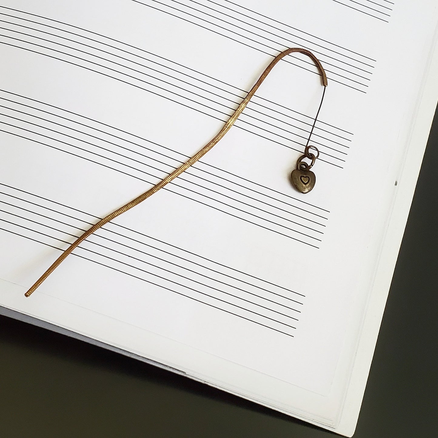 hook style bookmark made from an upcycled guitar string with a copper coloured heart shaped charm - background is blank sheet music