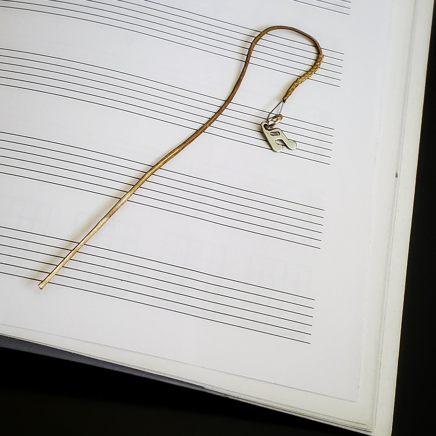 hook style bookmark made from an upcycled mandolin string and a silver quarter note shaped charm sitting on a blank page of sheet music