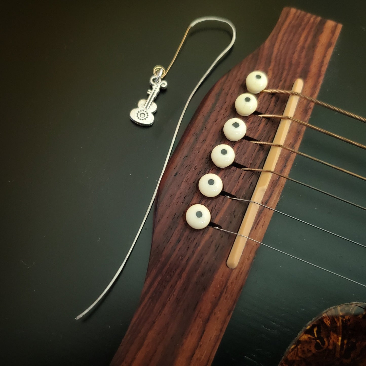 hook style bookmark made from an upcycled guitar string and a guitar shaped charm sitting on a black guitar