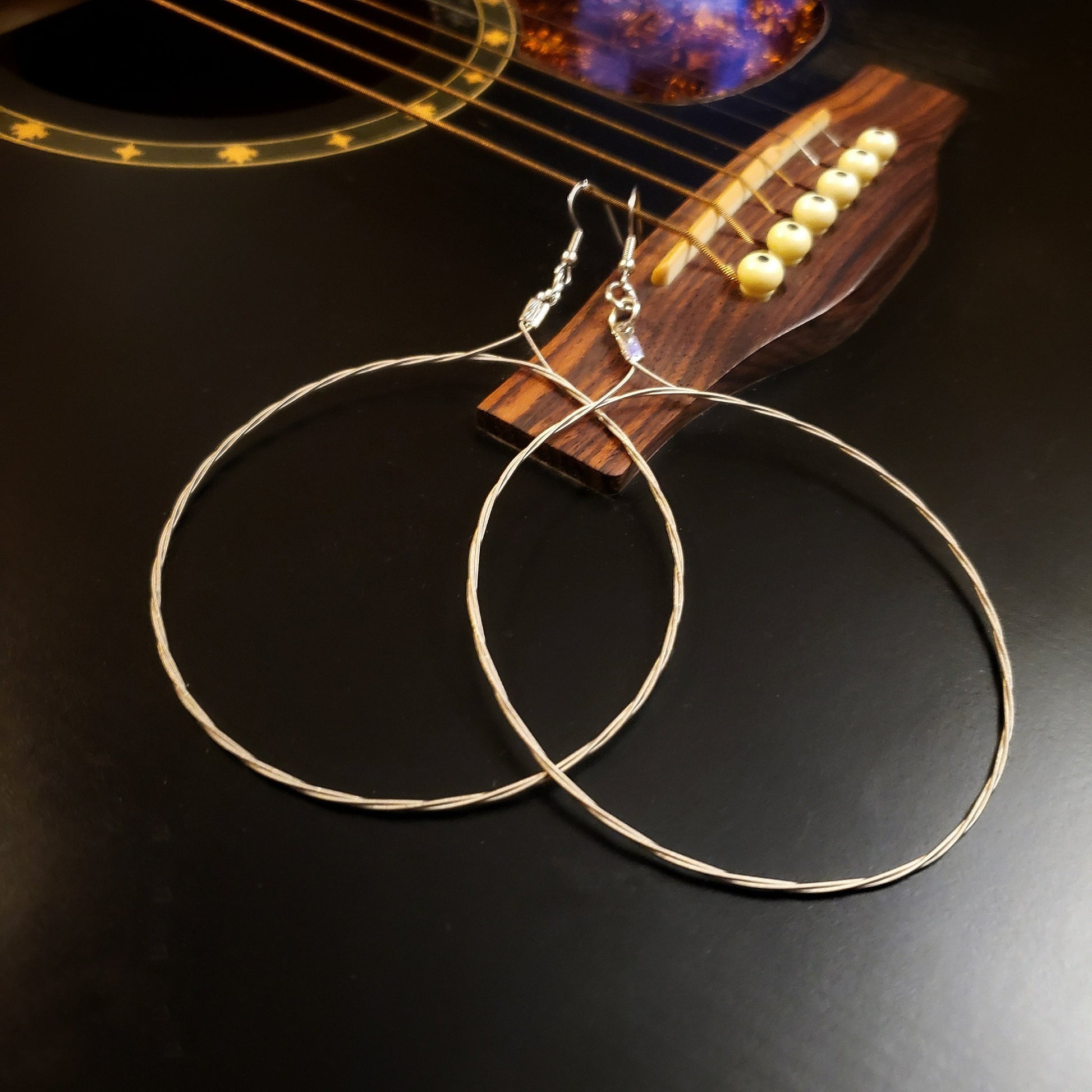 pair of large hoop style earrings made from upcycled guitar strings hooked onto a black guitar's E string