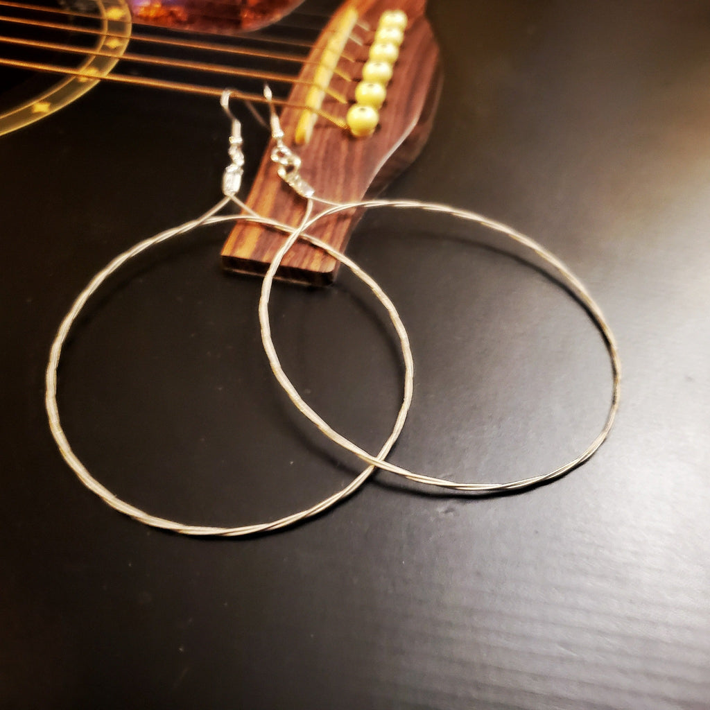 pair of large hoop style earrings made from upcycled guitar strings hooked onto a black guitar's E string