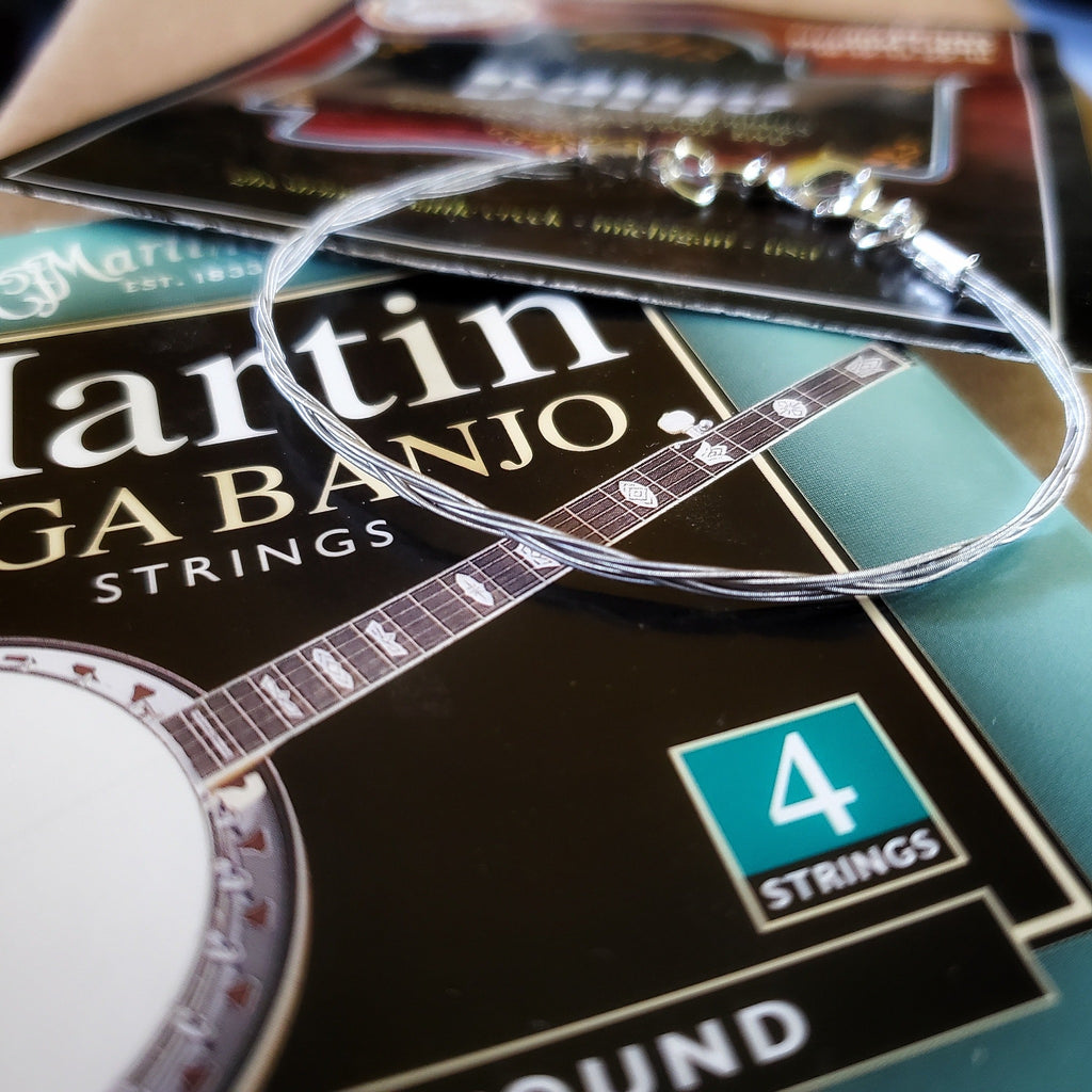 silver banjo string bracelet on a teal, black and red background with images of a banjo and the words Martin banjo strings, 4 strings.