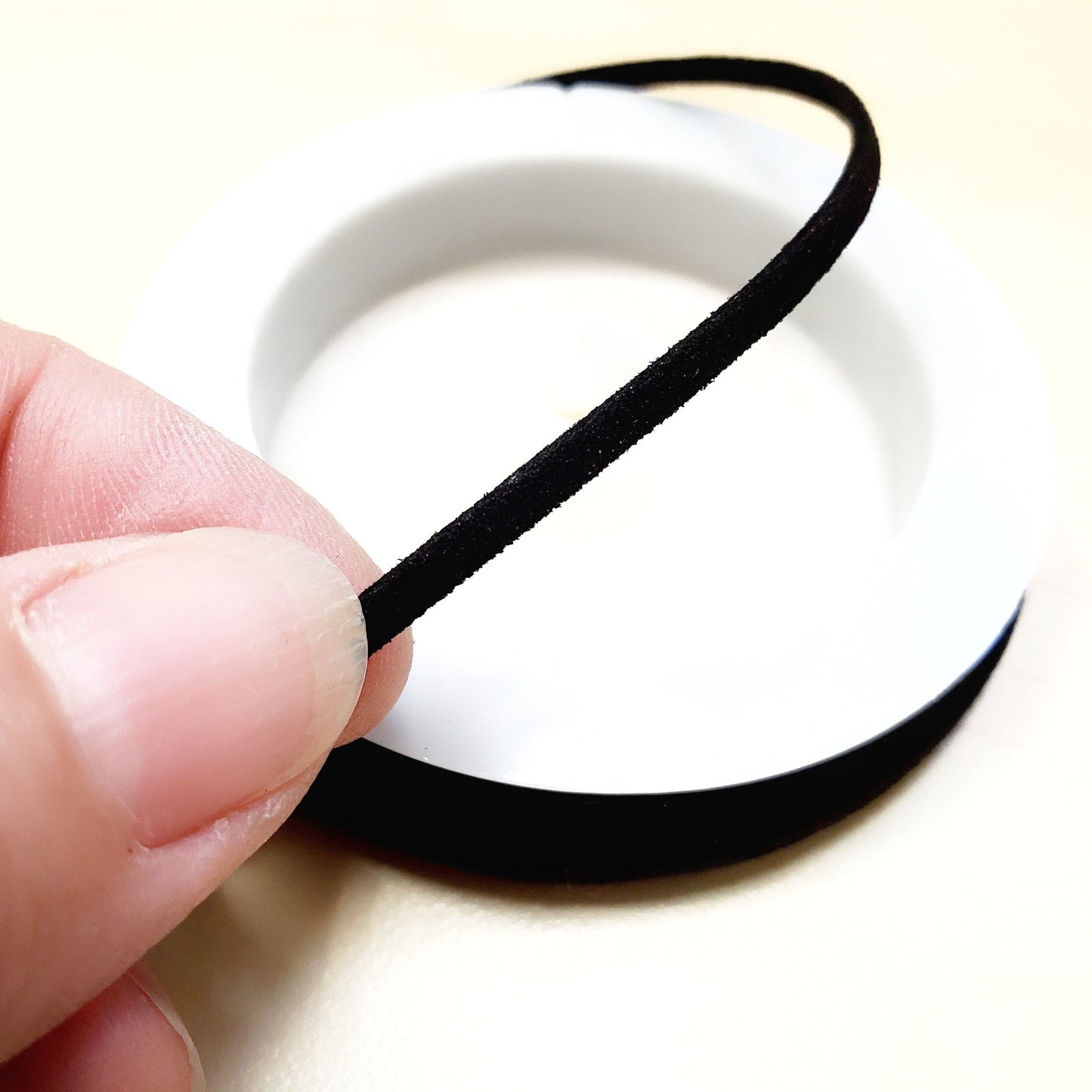 fingers holding a string of black faux-suede coming from a white bobbin