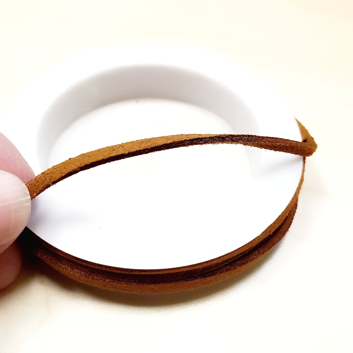 fingers holding a string of caramel brown faux-suede coming from a white bobbin