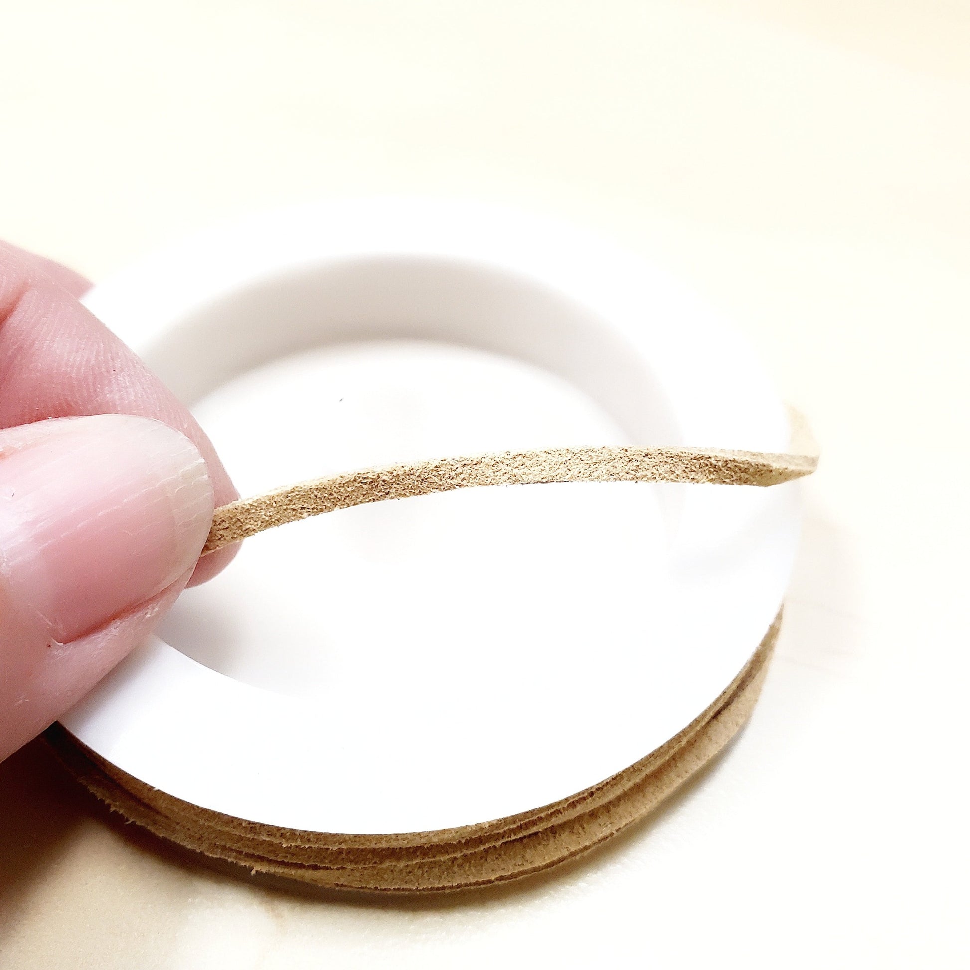 fingers holding a string of beige faux-suede coming from a white bobbin