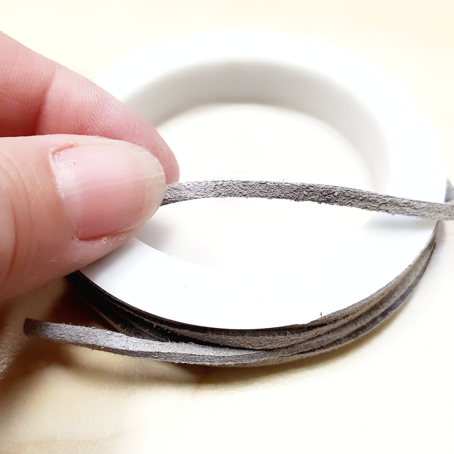fingers holding a string of grey faux-suede coming from a white bobbin