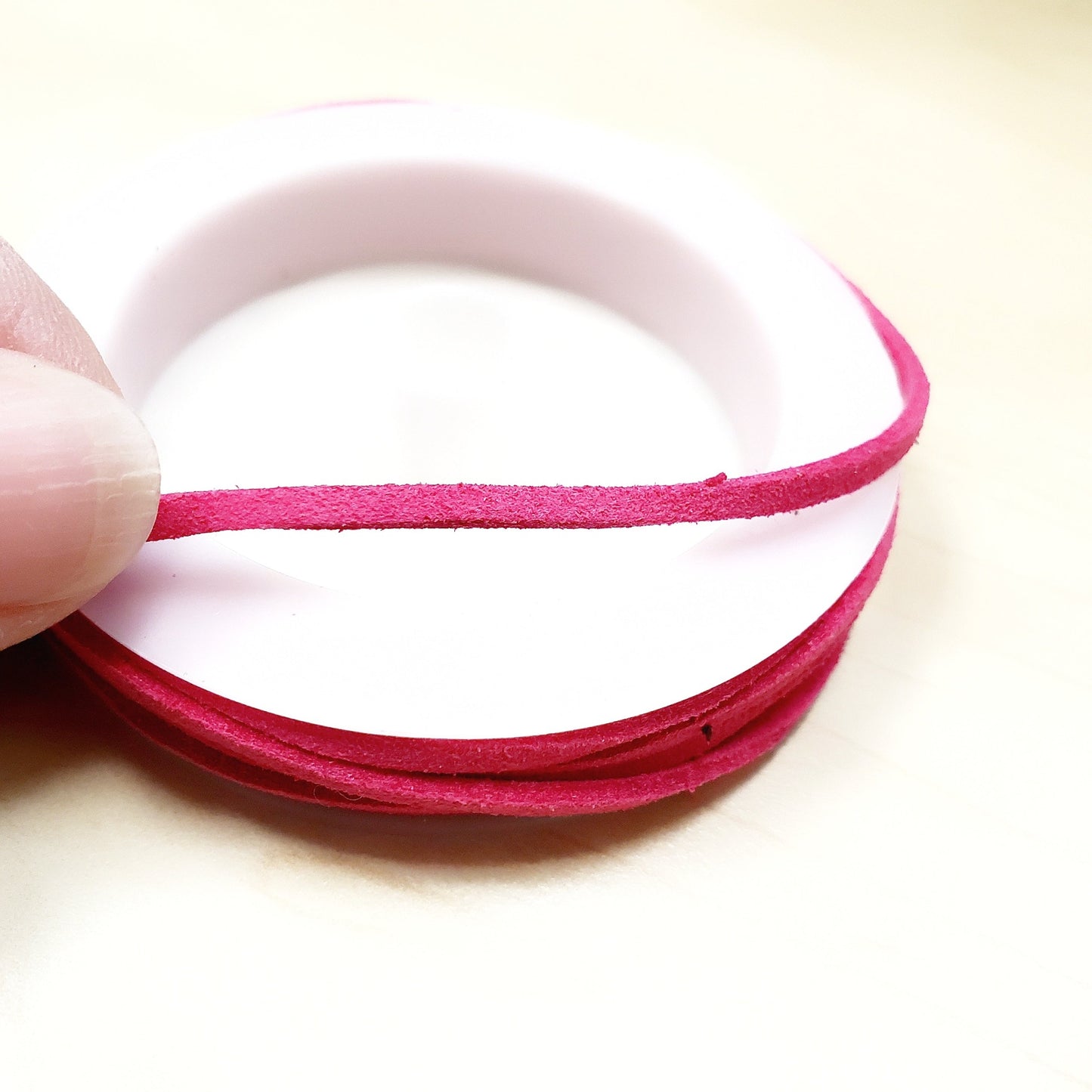 fingers holding a string of pink faux-suede coming from a white bobbin