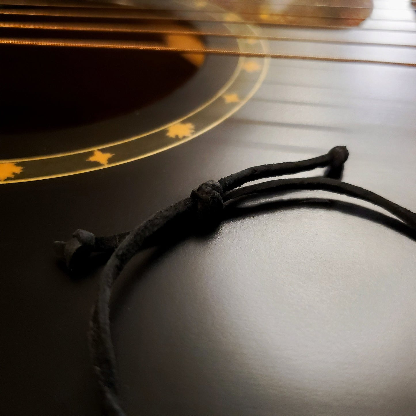 close-up of the knot of black bracelet made from a suede cord sitting on the neck of a black guitar